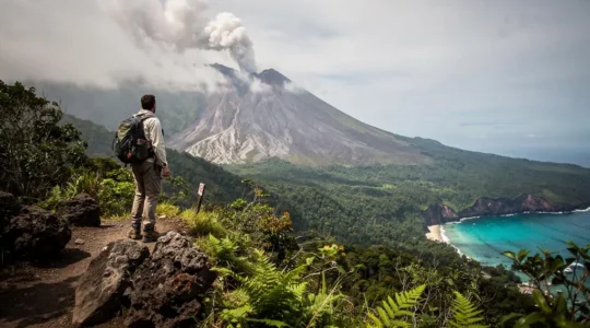 Randonneur contemplant un volcan tropical verdoyant surplombant la mer des Caraibes au lever du jour
