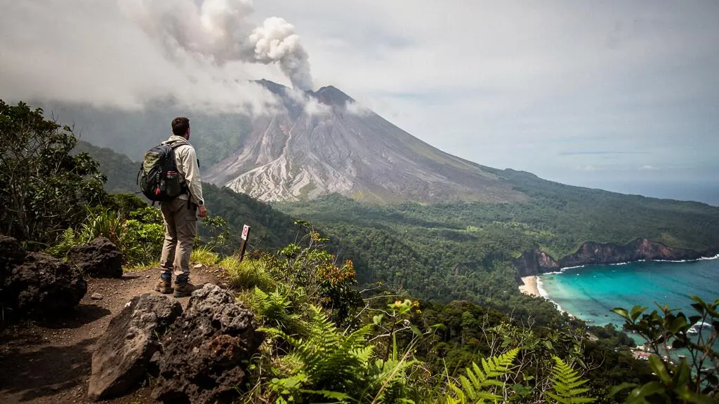Randonneur contemplant un volcan tropical verdoyant surplombant la mer des Caraibes au lever du jour